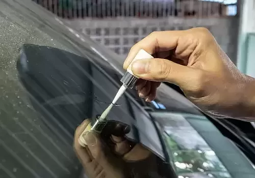 A man is cleaning the windshield of his car during a glass inspection from Glass Ding.